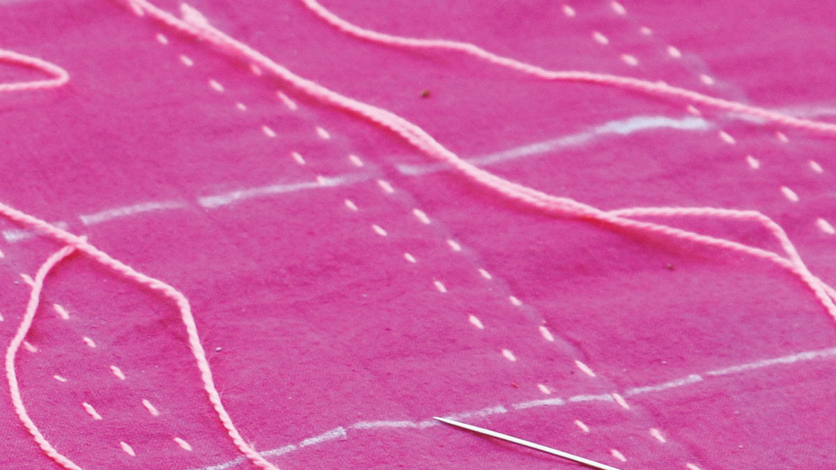 Close up of needle and pink thread sewing a pattern into magenta fabric