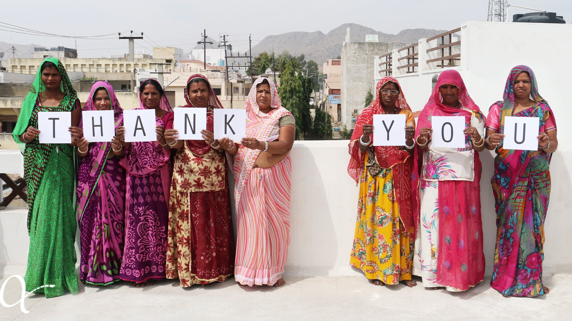 Eight artisan women standing in a line, each one holding up a letter to spell thank you in celebration of Anchal's gracious donors