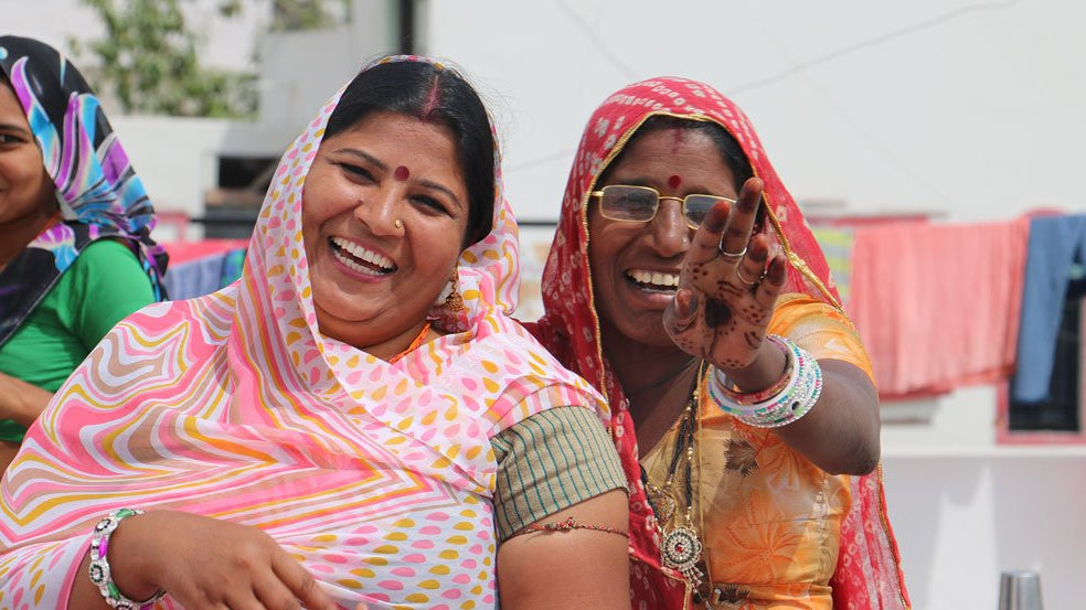 Two Indian women dressed in Sari's laughing with joyful expressions at an artisan workshop held by Anchal