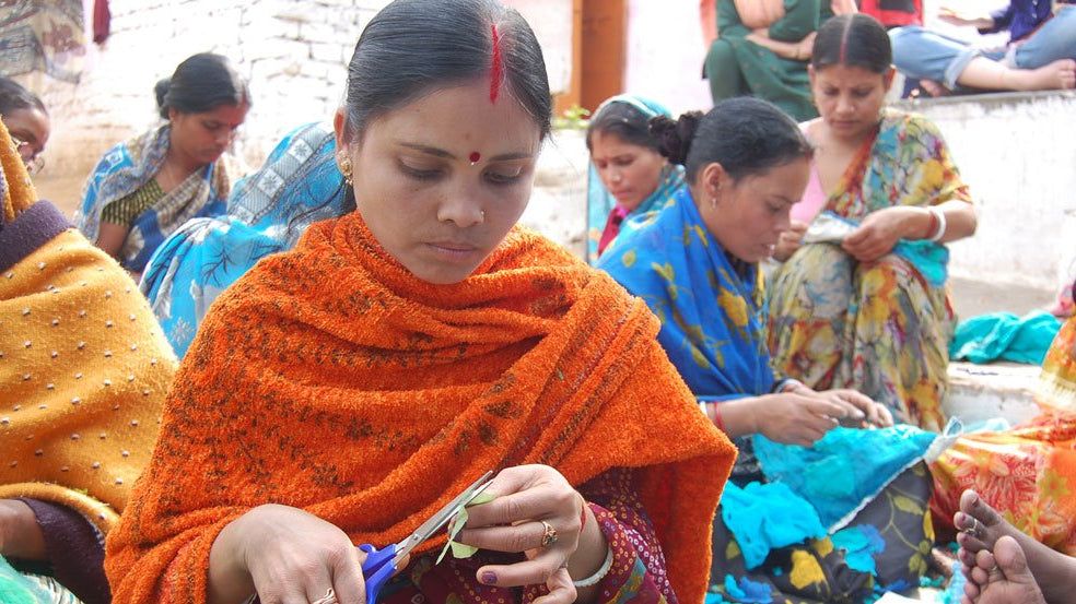 Artisan woman using scissors to cut a small piece of fabric for a project at an Anchal workshop