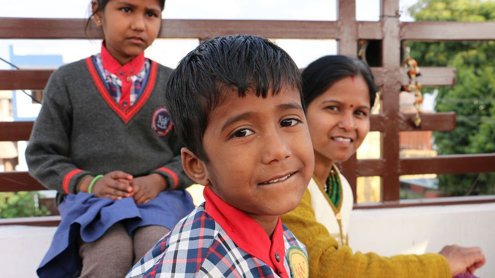 Two Indian children dressed in school uniform with an Indian woman, smiling at the camera