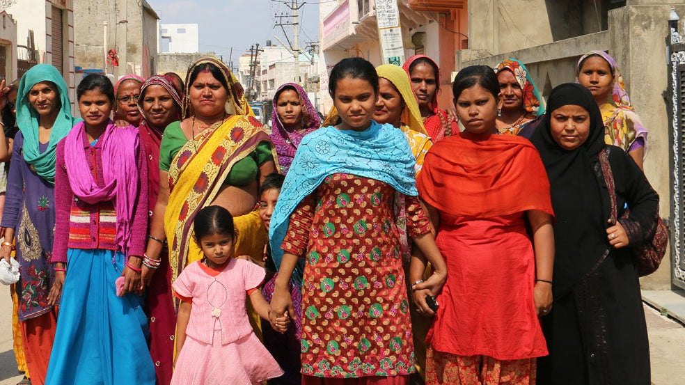 Large group of Indian women dressed in Sari's holding hands walking down the street