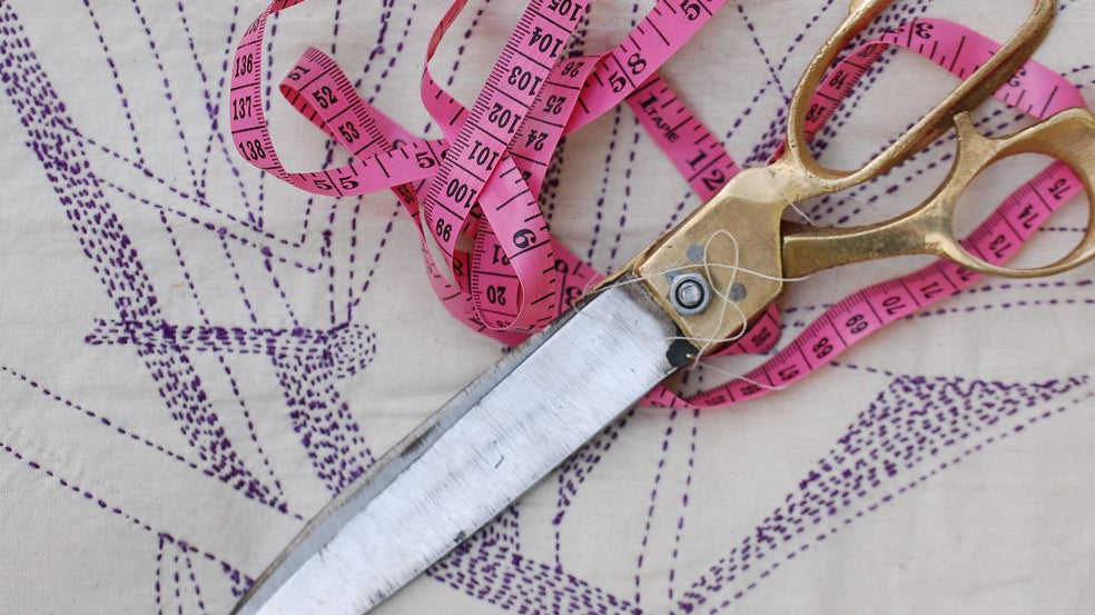 Scissors and a tape measure laying on top of an hand stitched design pattern