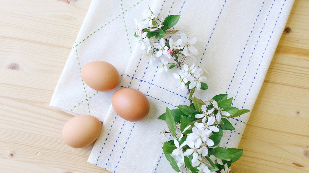 Three eggs and flowers laying on top of Anchal hand stitched tea towel
