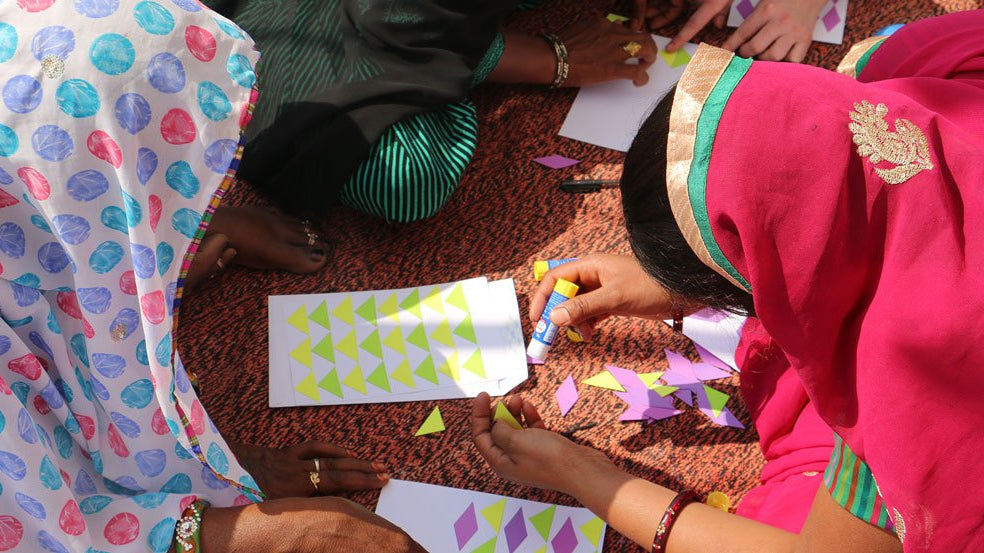 Two artisans creating triangle patterned art work by using small colored paper and glue