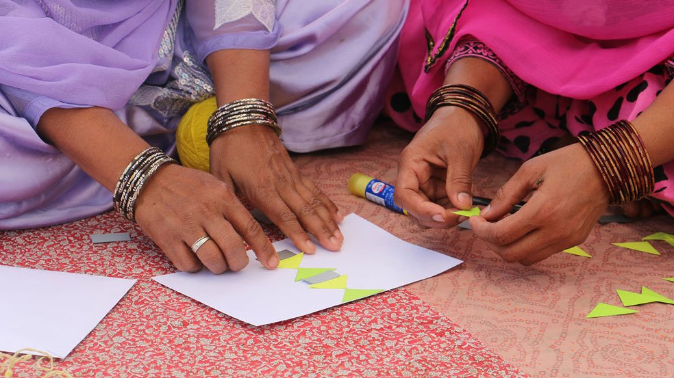 Anchal artisans glueing together colorful yellow pieces on paper to help spark inspiration for innovative new design patterns