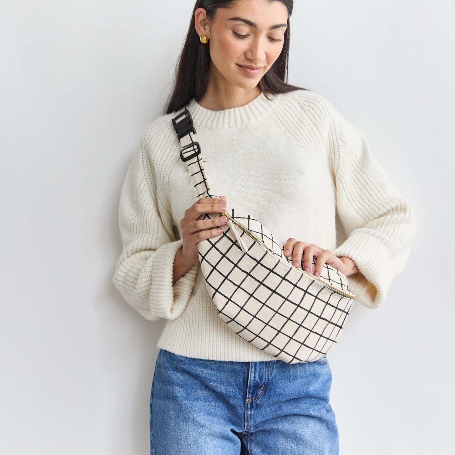 woman wearing white sweater with grid printed sling bag across chest in black and white