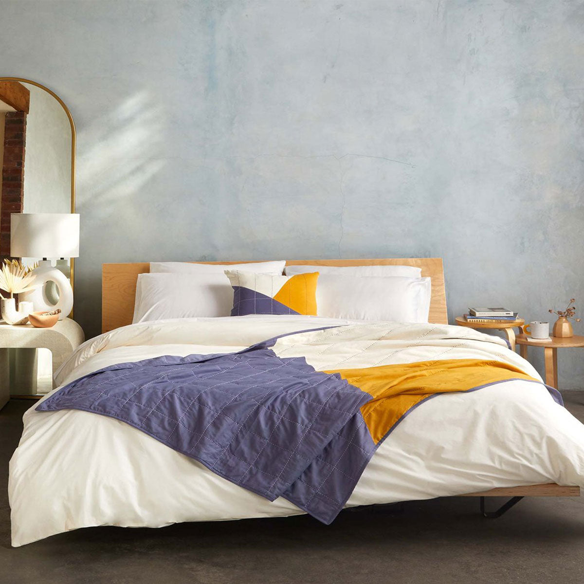 Anchal x Brooklinen collaboration featuring a patchwork quilt in blue, mustard yellow and white styled on an all white bed