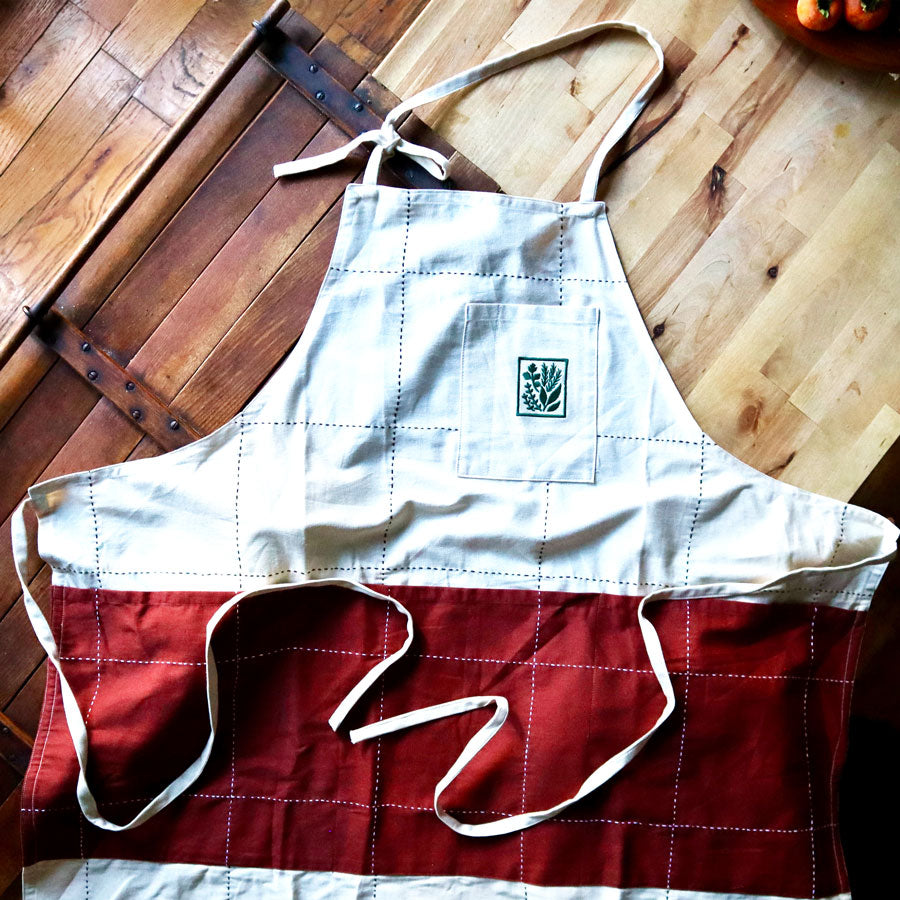 Anchal x Holly Hill white apron with rust red pockets and green embroidered logo on pocket