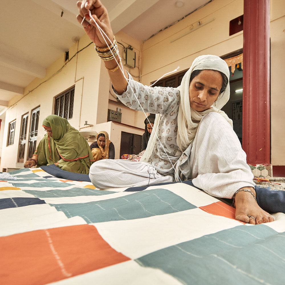 woman artisan hand sewing a colorful patchwork quilt with a needle and thread