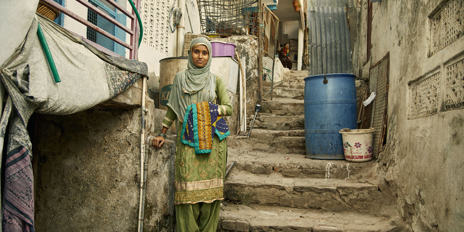woman standing with a small quilt outside of her home in Ajmer, India
