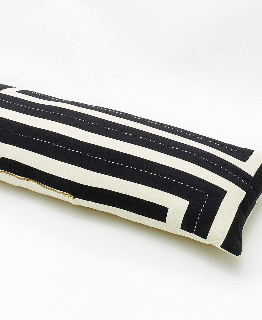 Black and white striped pillow with a gold zipper on a white background