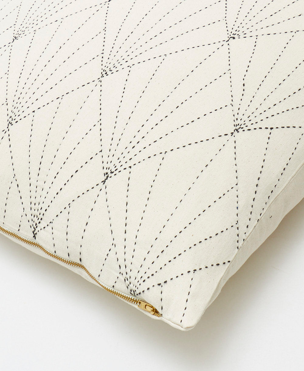 close-up detail of bone white throw pillow with black embroidery with a brass-tone exposed zipper closure