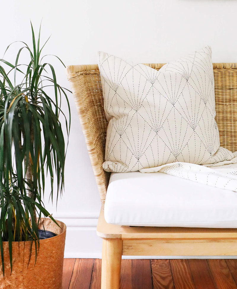 Wicker chair with a textured white pillow and a plant on a wooden floor