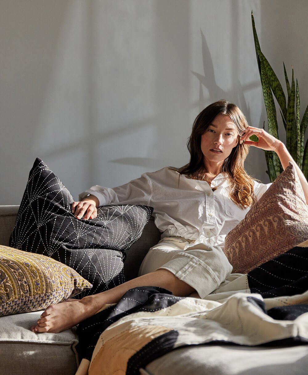 Woman sitting on a couch with decorative pillows and plants in the background