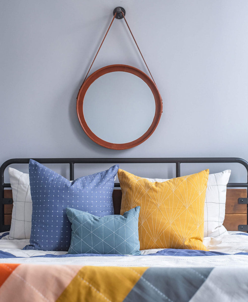 Bed with colorful pillows and a round mirror on the wall above