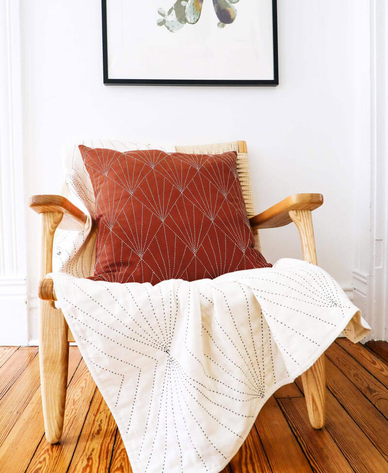 Wooden chair with a red pillow and white blanket in a room with a framed picture on the wall