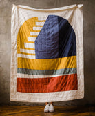 Colorful quilt with geometric pattern draped over a person against a plain background