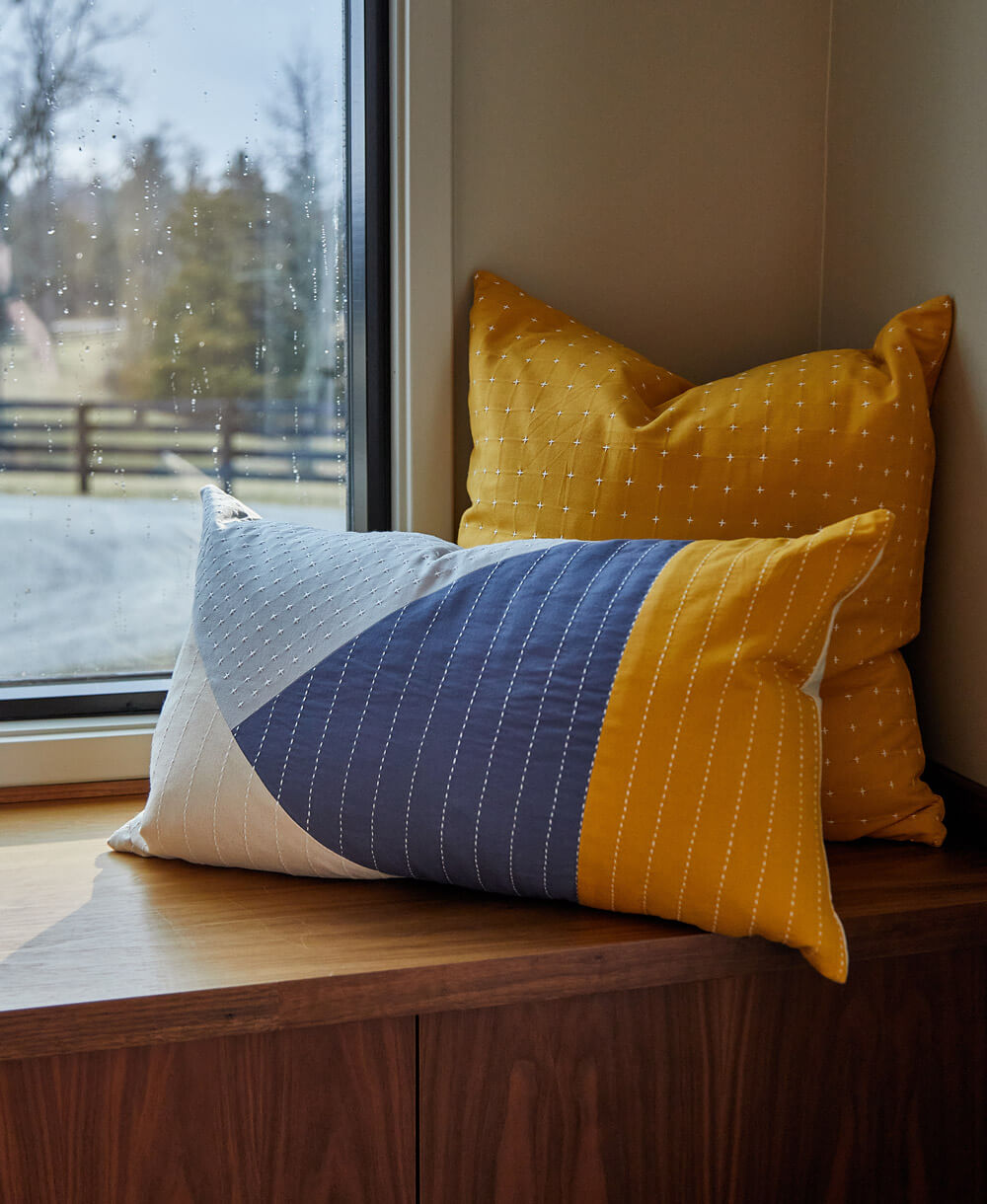 yellow and blue colorblock throw pillow sitting on window sill bench with white emboridery