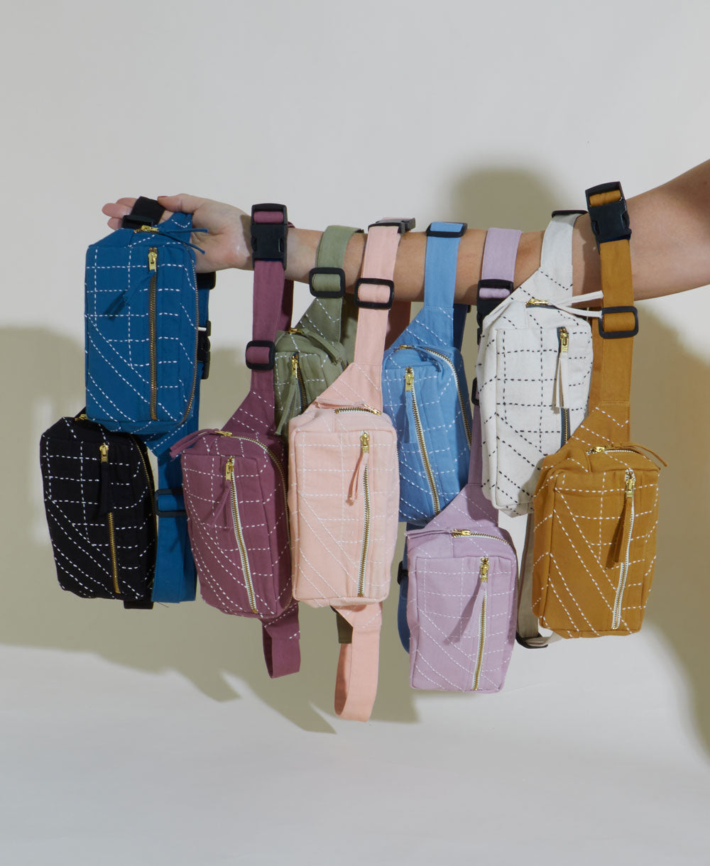 Hand holding multiple colorful waist bags against a neutral background