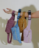 Four colorful bags hanging from a person's arm against a plain background