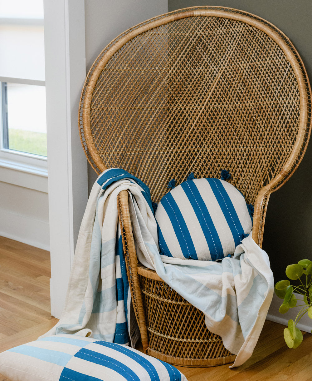 Wicker chair with blue and white striped cushions and a blanket in a room with a window