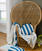 Wicker chair with blue and white striped cushions and a blanket in a room with a window