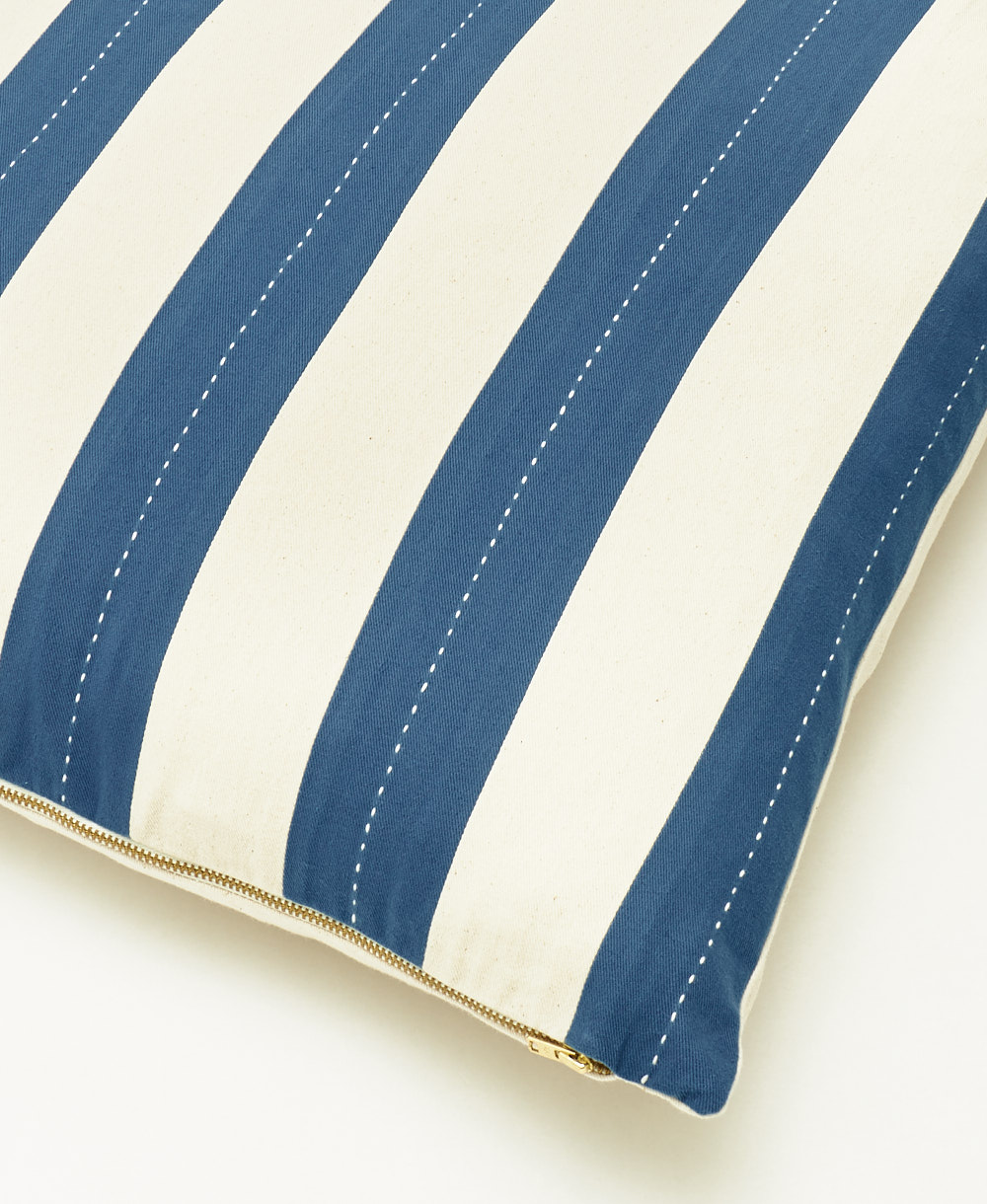 Close-up of a blue and white striped pillow with a gold zipper on a light background
