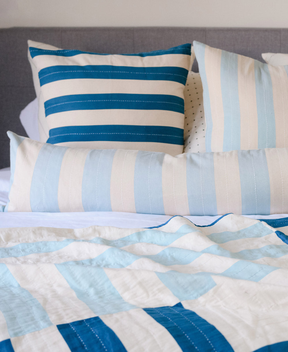 Blue striped pillows and a patchwork quilt on a bed with a gray headboard