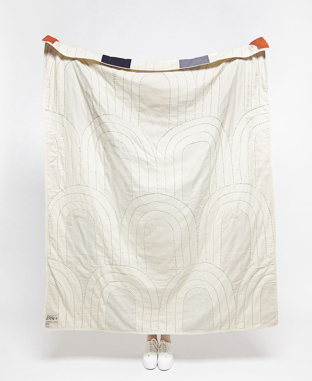 White quilt with geometric pattern draped over a person on a white background