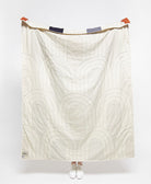 White quilt with geometric pattern draped over a person on a white background