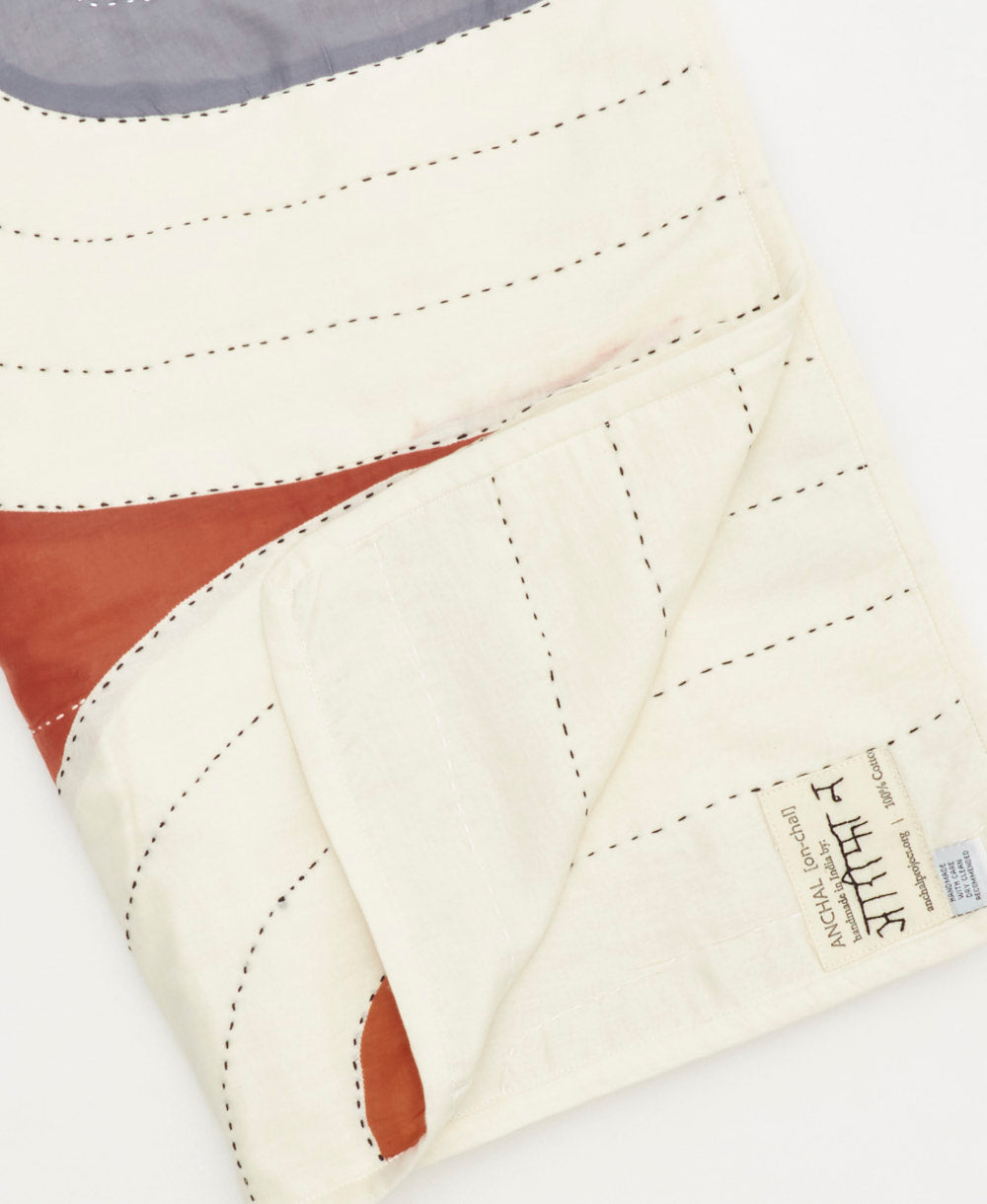 Close-up of a quilt with visible stitching and a brand label on a white background
