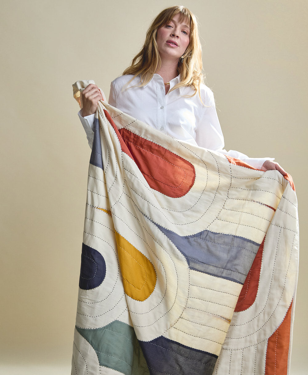 Woman holding a colorful patchwork quilt with geometric patterns against a plain background