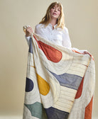 Woman holding a colorful patchwork quilt with geometric patterns against a plain background