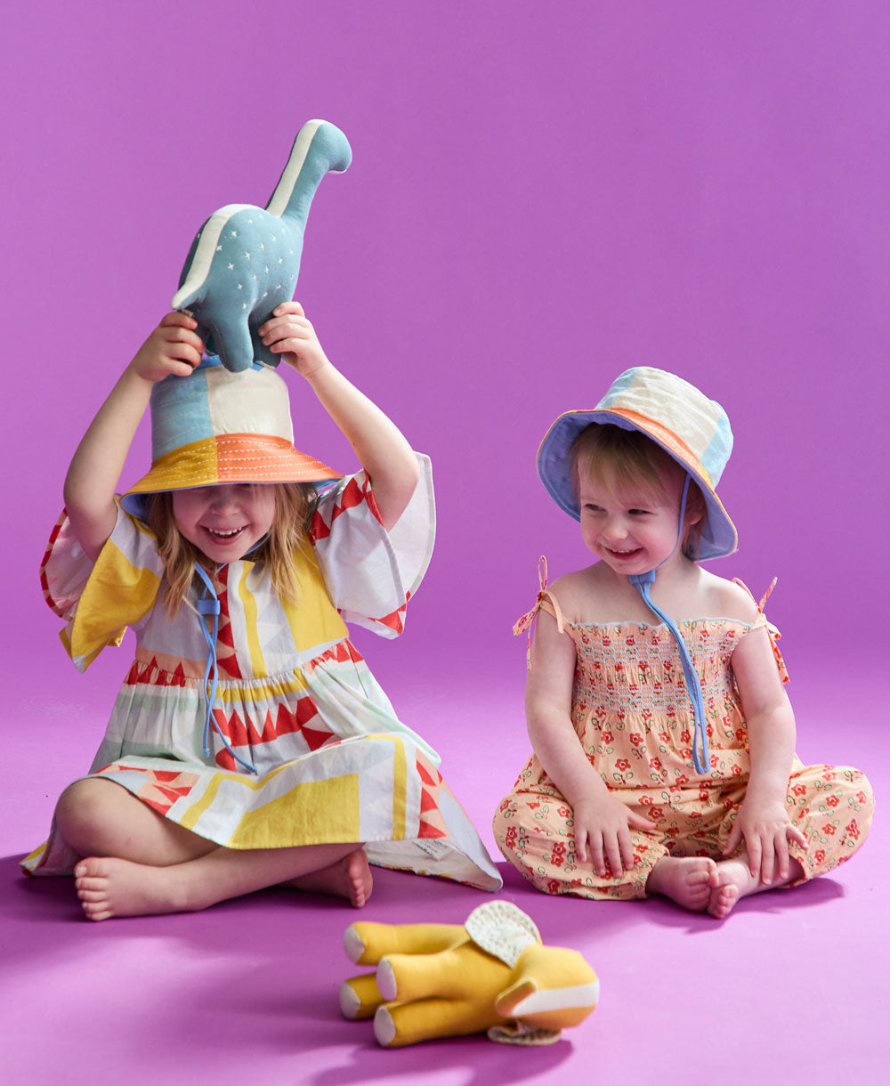 two little girls sitting on the floor playing with stuffed animals wearing colorful checkered bucket hats