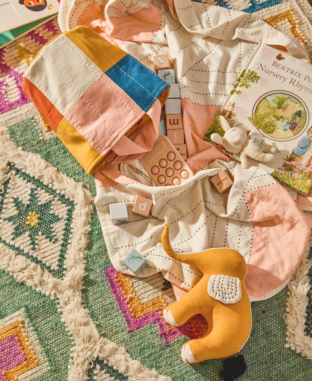 Patchwork blanket with toys and a book on a textured surface