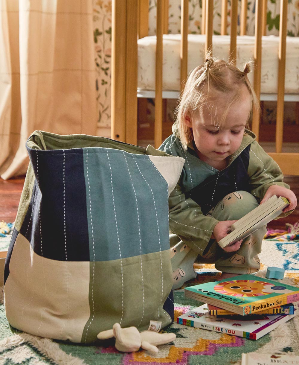 Child playing with books and toys near a colorful storage bin in a room