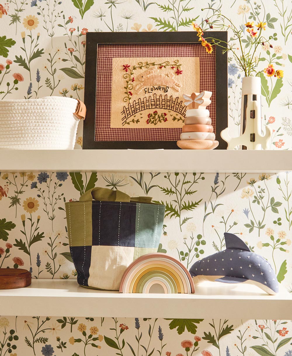 Decorative shelf with framed artwork, stack of books, and decorative items against a floral wallpaper background