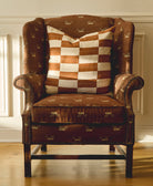 Brown upholstered armchair with a checkered pillow in a room with light-colored walls and wooden floor