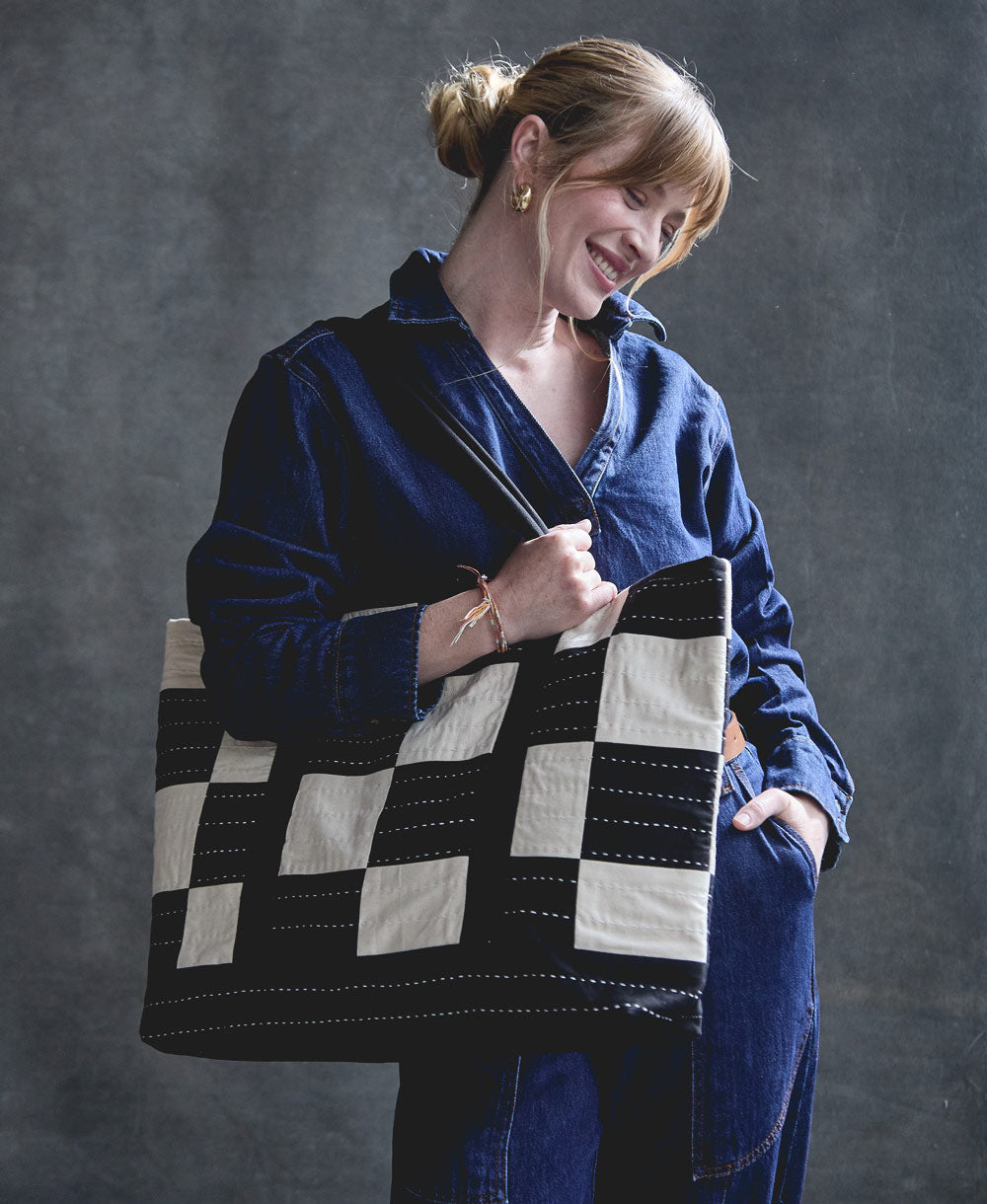 woman carrying a black and white checkered tote bag over her shoulder with white horizontal embroidery