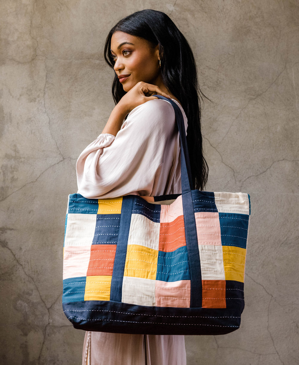 colorful checkered tote bag draped over woman's shoulder with navy blue shoulder strap