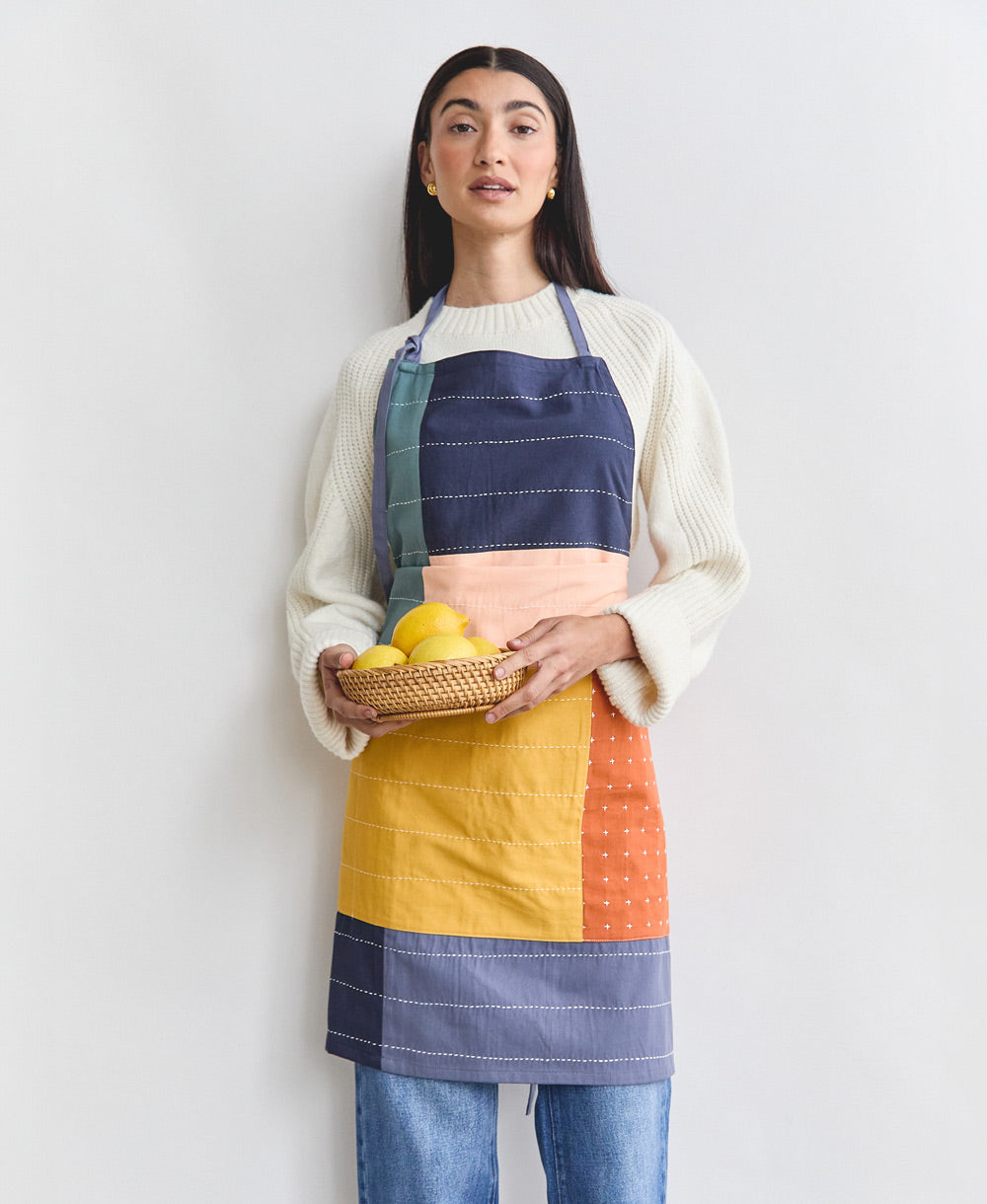 Woman wearing a colorful apron holding a basket of lemons against a white background