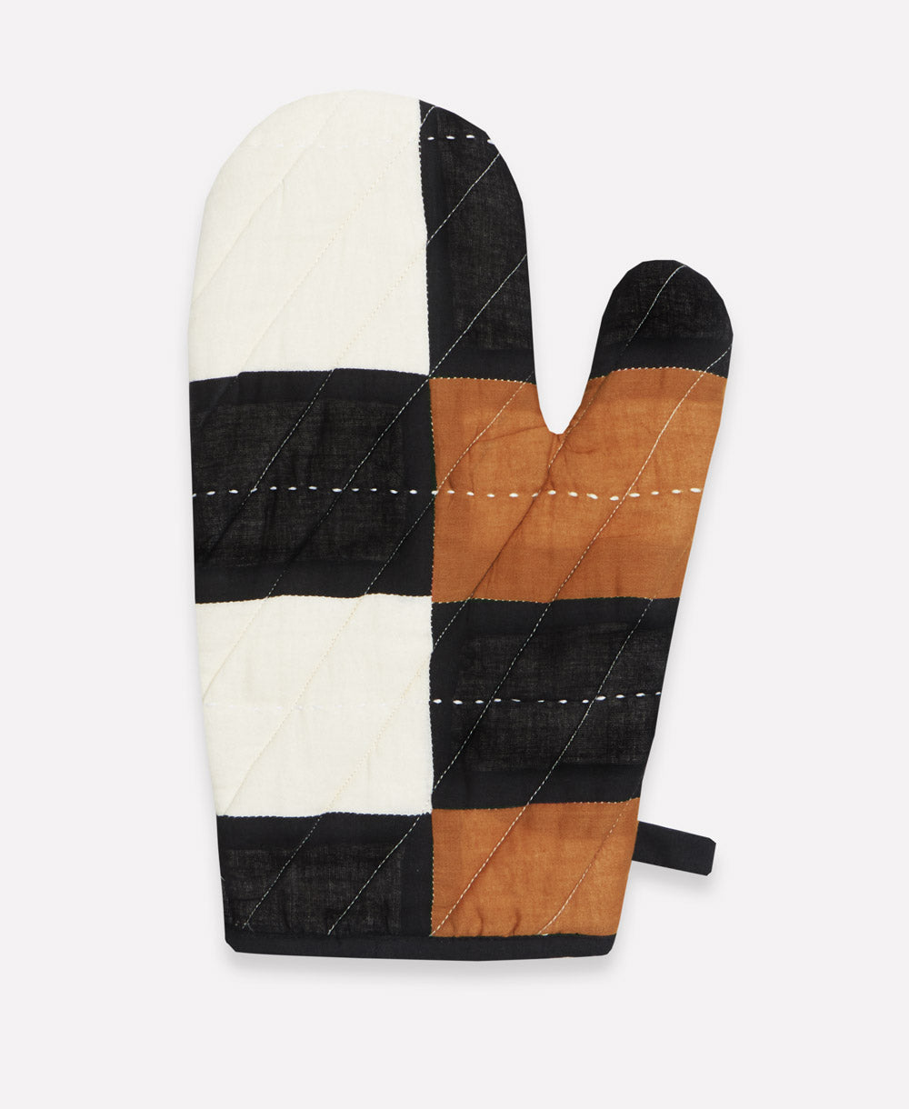 Patchwork oven mitt with black, brown, and white squares on a light gray background