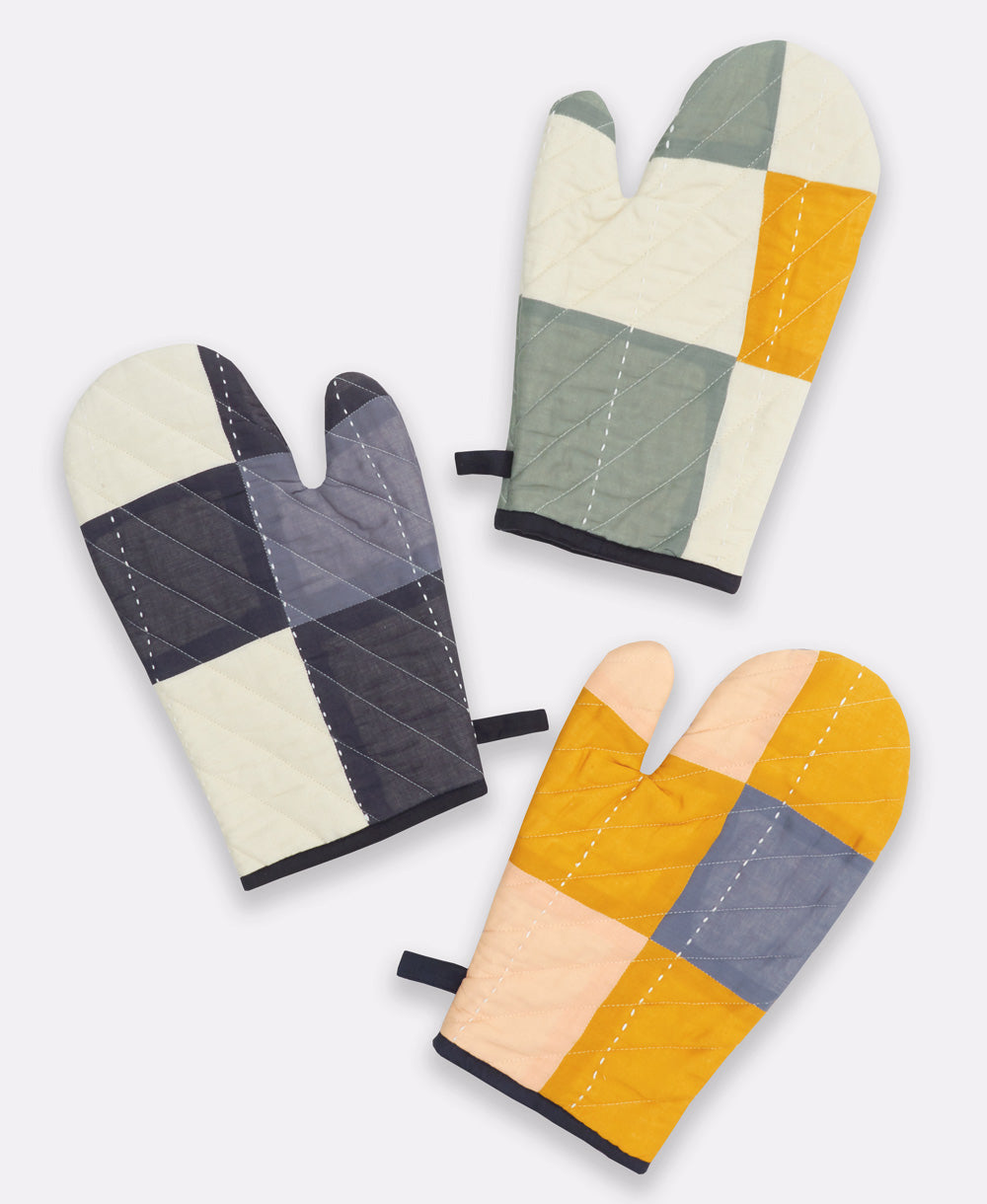 Three patchwork oven mitts in different color patterns on a white background