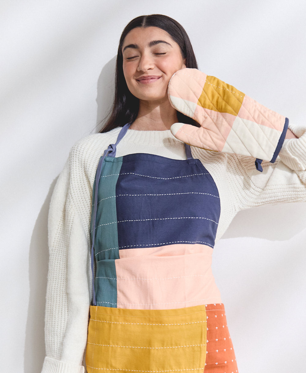 Person wearing a colorful patchwork apron and oven mitt on a white background