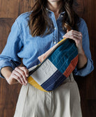 checkered sling crossbody bag worn across the body with a fabric zipper pull made from 100% organic cotton