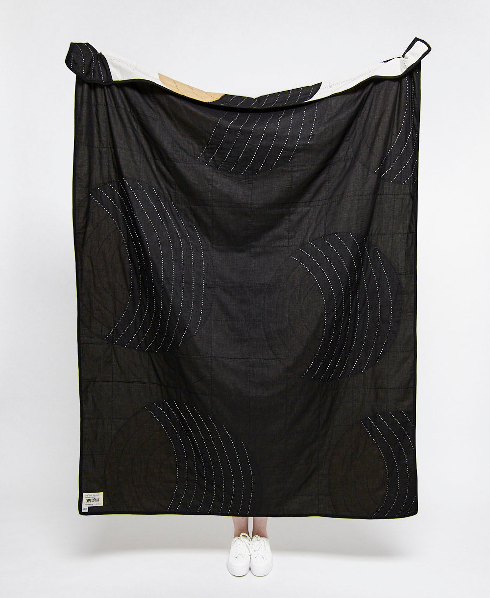 Black quilt with geometric pattern draped over a person on a white background