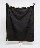 Black quilt with geometric pattern draped over a person on a white background