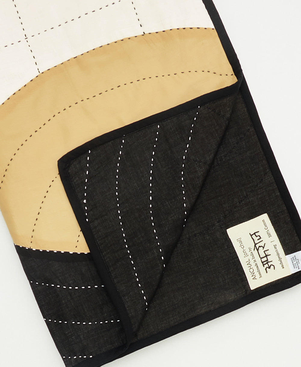 Close-up of a black and beige quilt with visible stitching and a brand label on a white background.