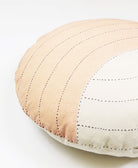 Quilted round pillow with beige and white color block design on a light background
